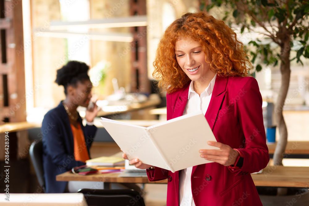 Woman holding white notebook standing in the office Woman holding white notebook standing in the office
