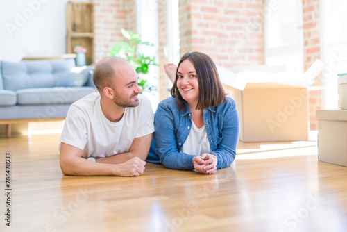 Young couple in love lying on the floor of new house arround cardboard boxes, smiling very happy for moving to a new apartment