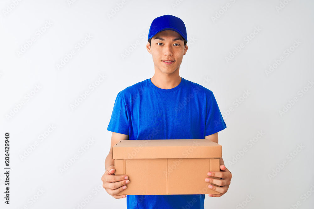 Chinese deliveryman wearing cap holding box standing over isolated white background with a happy face standing and smiling with a confident smile showing teeth Chinese deliveryman wearing cap holding box standing over isolated white background with a happy face standing and smiling with a confident smile showing teeth