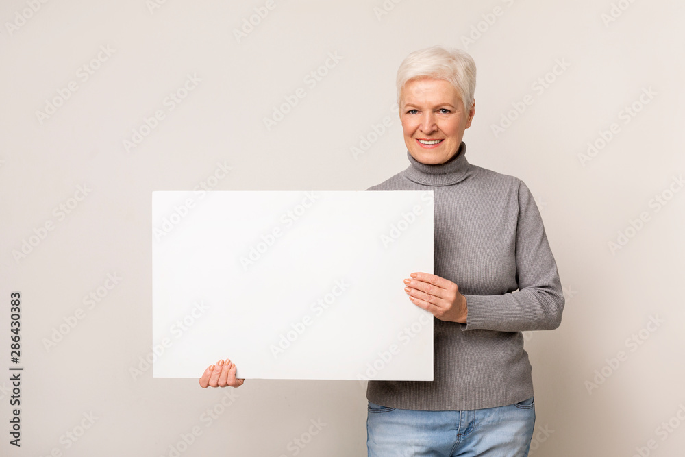 Mature woman with blank advertising board over light studio background