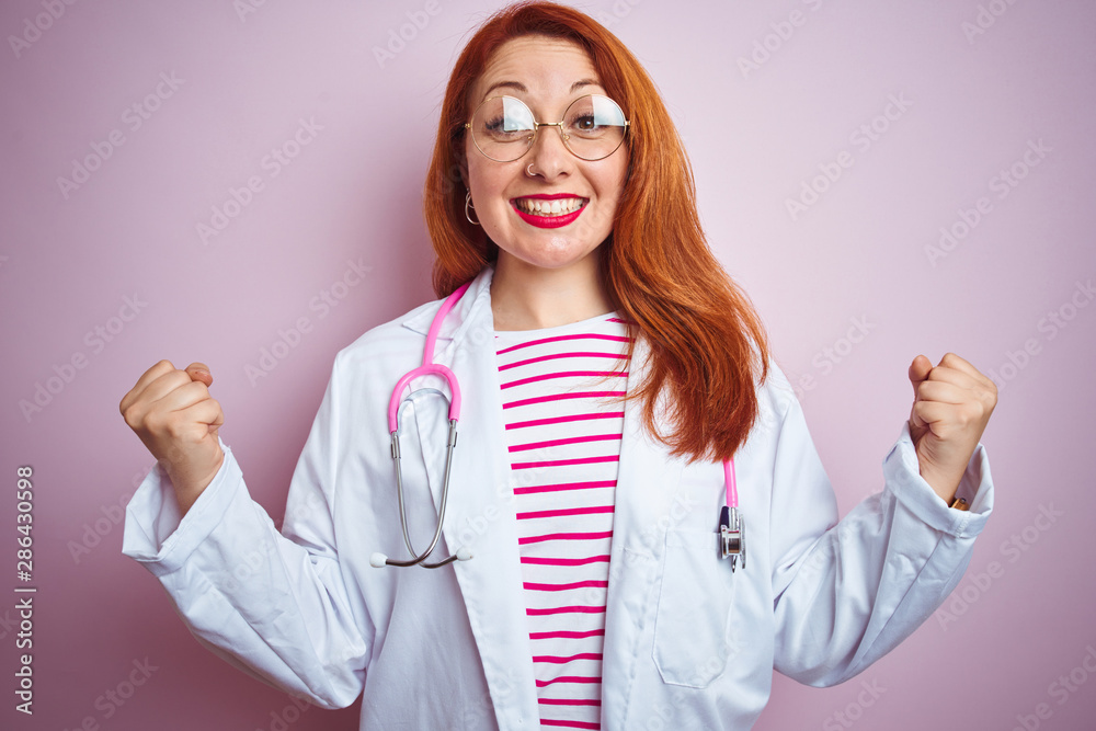 Young redhead doctor woman wearing glasses over pink isolated background celebrating surprised and amazed for success with arms raised and open eyes. Winner concept.