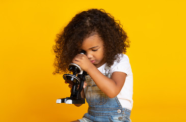 Kid girl looking through microscope, yellow background