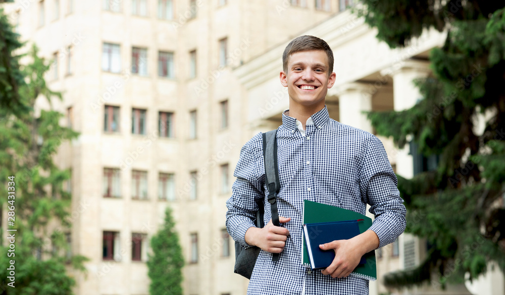 Happy guy student waiting for lessons near university outdoor