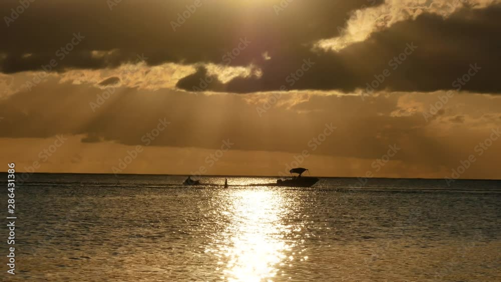 A sportboat pulling a big float with people in it passsing over the sunlight reflected under light rays
passing through the clouds A sportboat pulling a big float with people in it passsing over the sunlight reflected under light rays
passing through the clouds