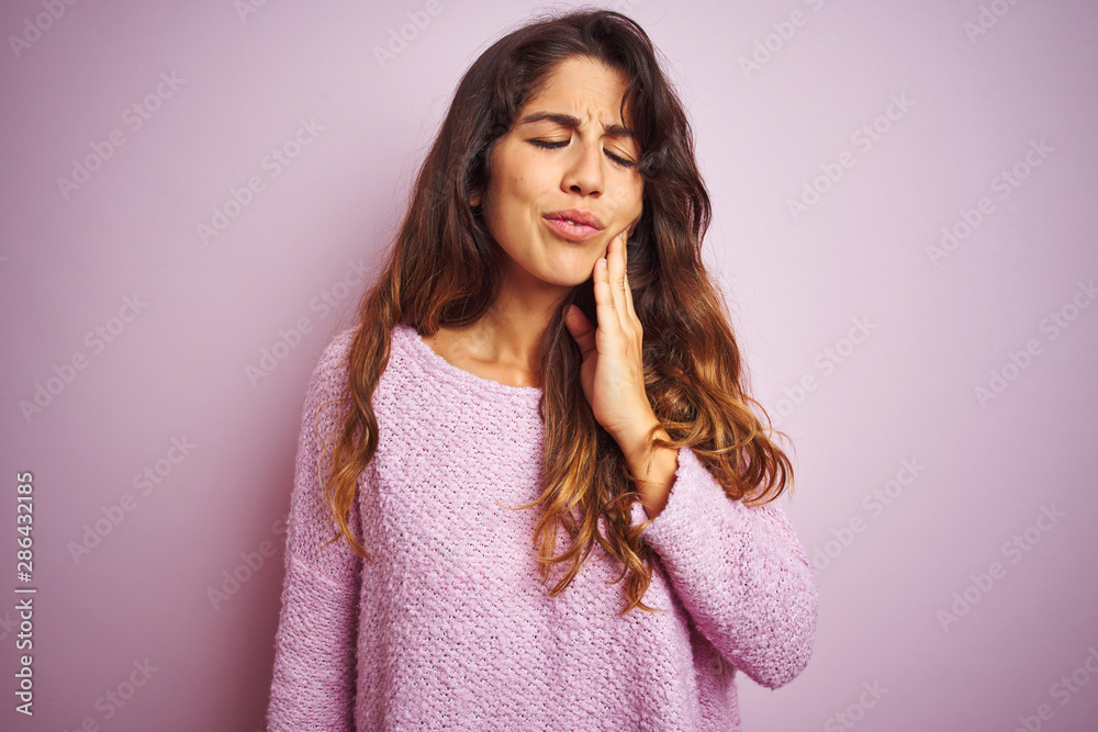 Young beautiful woman wearing sweater standing over pink isolated background touching mouth with hand with painful expression because of toothache or dental illness on teeth. Dentist concept. Young beautiful woman wearing sweater standing over pink isolated background touching mouth with hand with painful expression because of toothache or dental illness on teeth. Dentist concept.