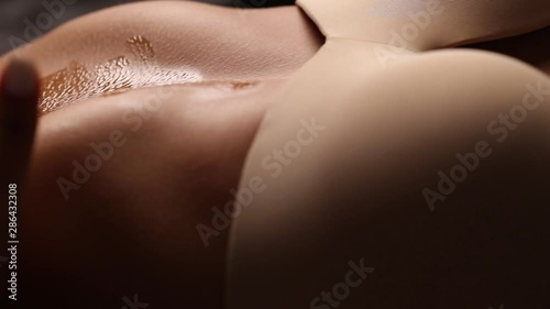 Beautiful female belly with drops of oil on a black background. Flesh-colored underwear. Cosmetic oil on a woman's body. Hard breath.