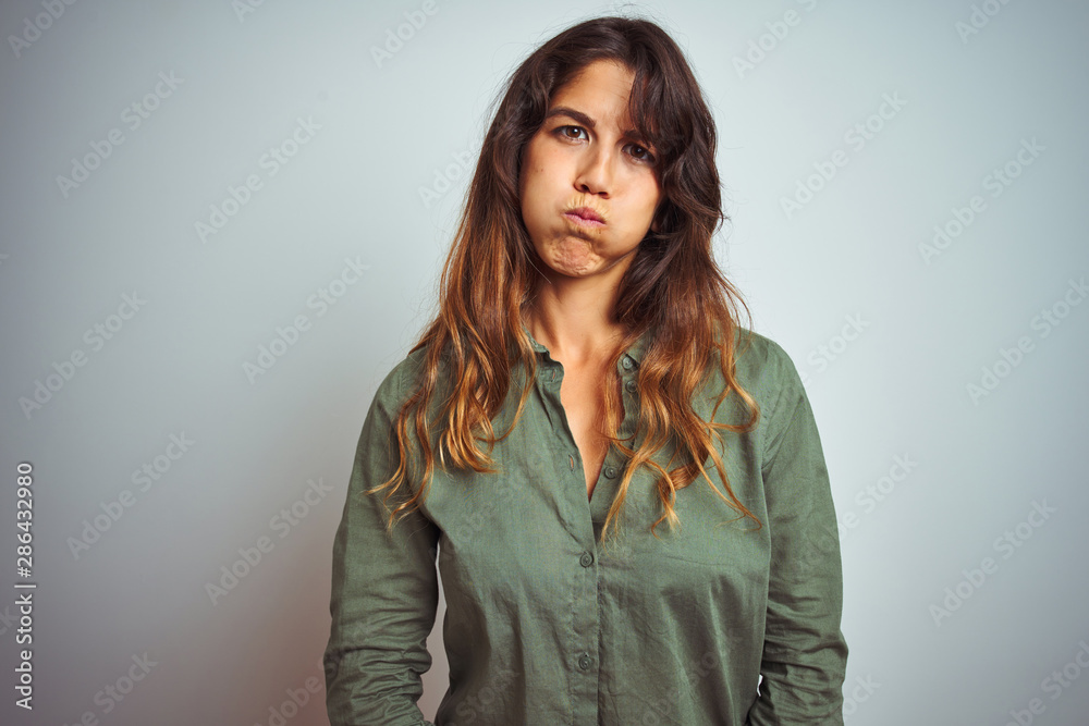 Young beautiful woman wearing green shirt standing over grey isolated background puffing cheeks with funny face. Mouth inflated with air, crazy expression. Young beautiful woman wearing green shirt standing over grey isolated background puffing cheeks with funny face. Mouth inflated with air, crazy expression.