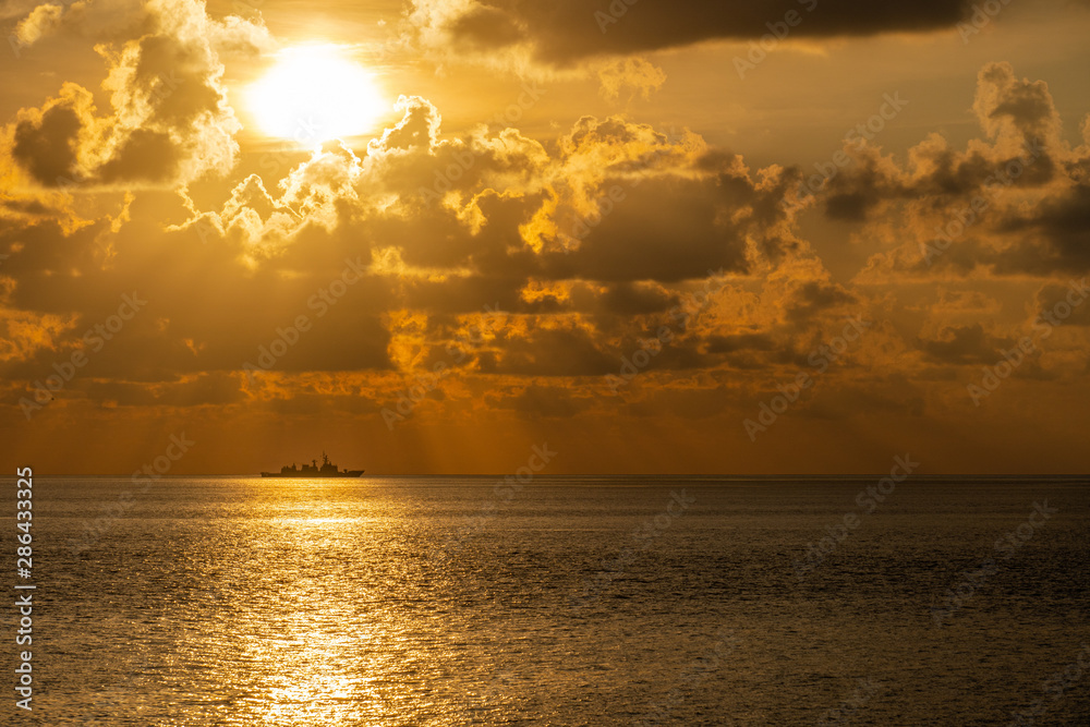 Silhouette of a warship maybe frigate or destroyer sails along the trade route to protect national resources from illegal activities at sea when the evening before sunset.