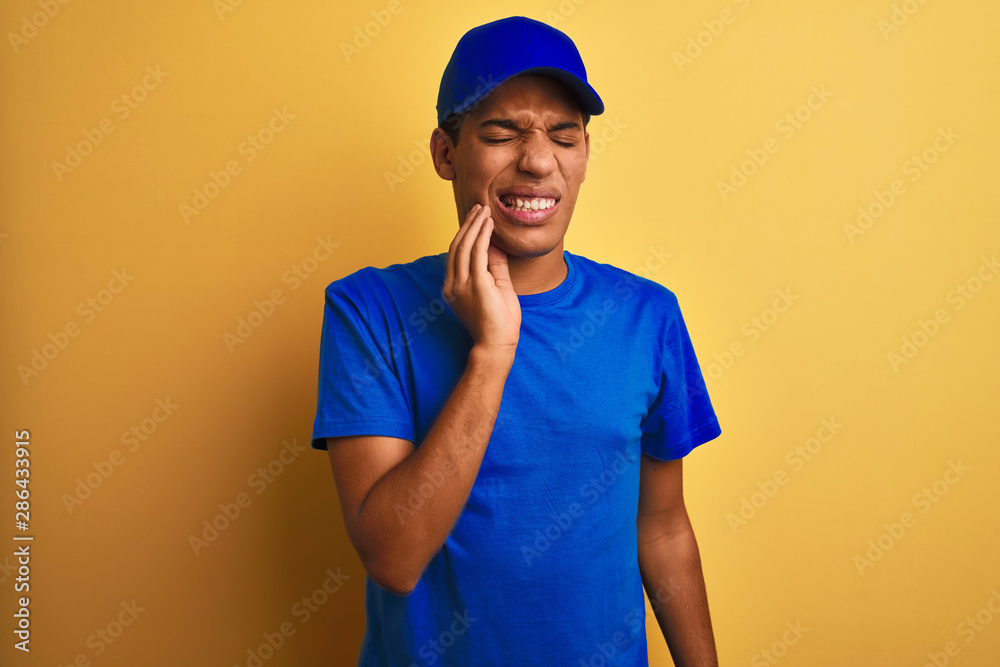 Young handsome arab delivery man standing over isolated yellow background touching mouth with hand with painful expression because of toothache or dental illness on teeth. Dentist concept.