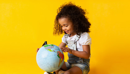 Cute little girl looking at earth globe, yellow background