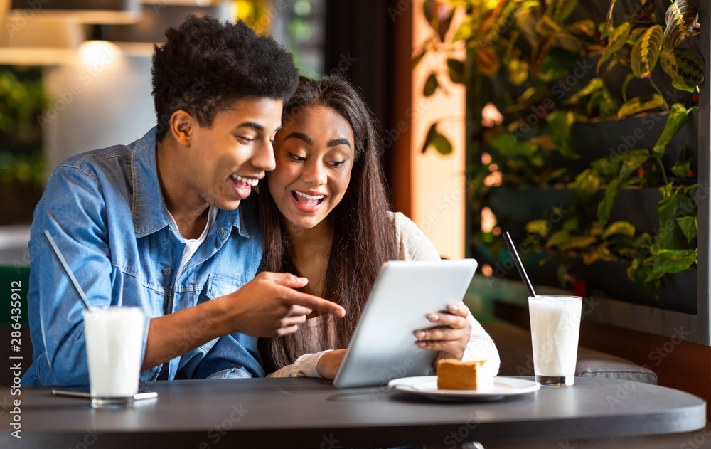 Flirting couple in cafe using digital tablet and laughing