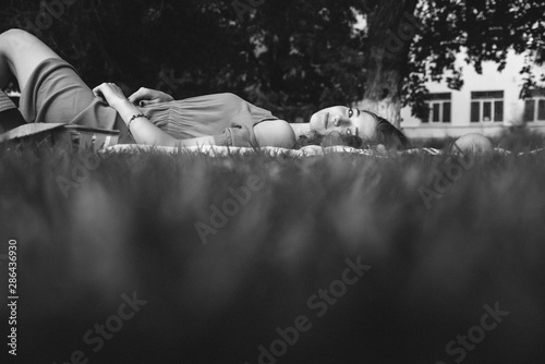 A young woman lies in a park on a picnic on a plaid and looks at the camera