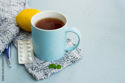 Cold and flu season. Cup with hot tea, lemon, mint, thermometer and tablets on a light background. Treatment and prevention of the virus. Copy space