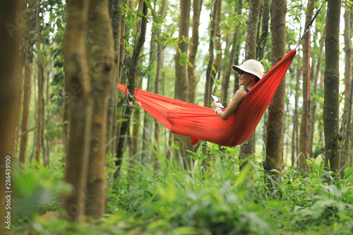 Woman relaxing in hammock with smartphone in tropical rainforest
