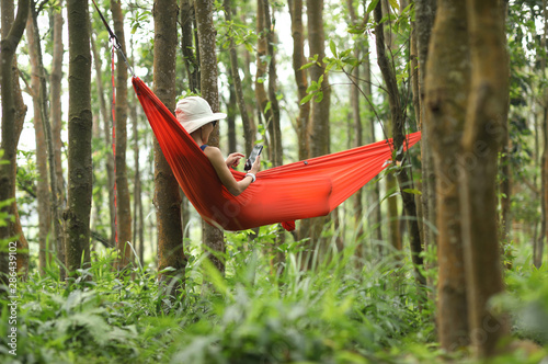 Woman relaxing in hammock with smartphone in tropical rainforest