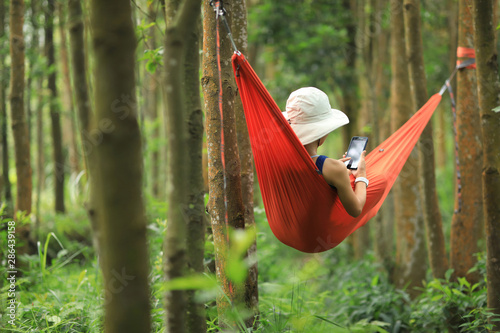 Woman relaxing in hammock with smartphone in tropical rainforest