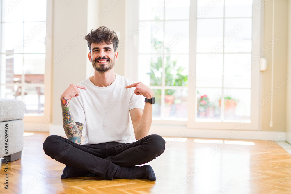 Young man working sitting casual on the floor at home looking confident with smile on face, pointing oneself with fingers proud and happy. Young man working sitting casual on the floor at home looking confident with smile on face, pointing oneself with fingers proud and happy.