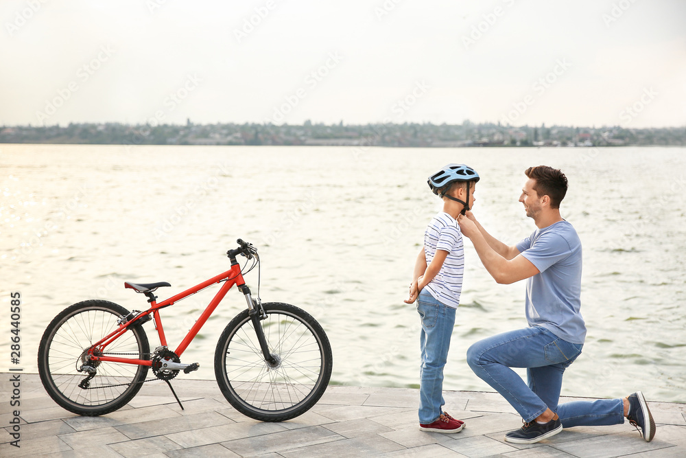 Fototapeta premium Father helping his son to put on helmet before riding bicycle outdoors