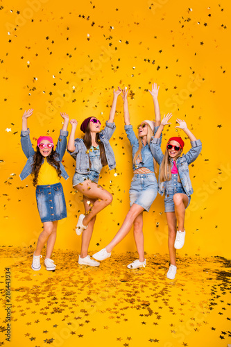 Vertical full length size body photo of four beautiful cheerful ecstatic excited positive charming people girlfriends having funky fancy vacation and rest chilling out isolated yellow background