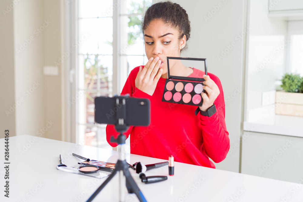 Young african american influencer woman recording make up tutorial cover mouth with hand shocked with shame for mistake, expression of fear, scared in silence, secret concept Young african american influencer woman recording make up tutorial cover mouth with hand shocked with shame for mistake, expression of fear, scared in silence, secret concept