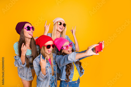 Close-up photo of cool carefree charming nice ladies showing tongue-out heavy metal symbols small photographer taking self picture of fellow friendship group people isolated yellow background