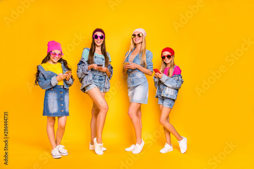 Full length photo of four nice positive cool millennials using modern technology following stars users on social network browsing reading news isolated yellow background