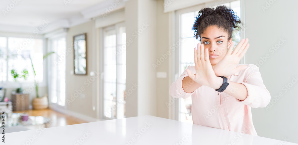 Wide angle of beautiful african american woman with afro hair Rejection expression crossing arms and palms doing negative sign, angry face Wide angle of beautiful african american woman with afro hair Rejection expression crossing arms and palms doing negative sign, angry face