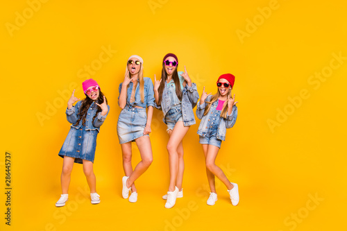 Full length body photo of group of four carefree careless best girlfriends feeling good style having perfect colorful caps wearing denim skirts showing heavy metal symbol isolated yellow background