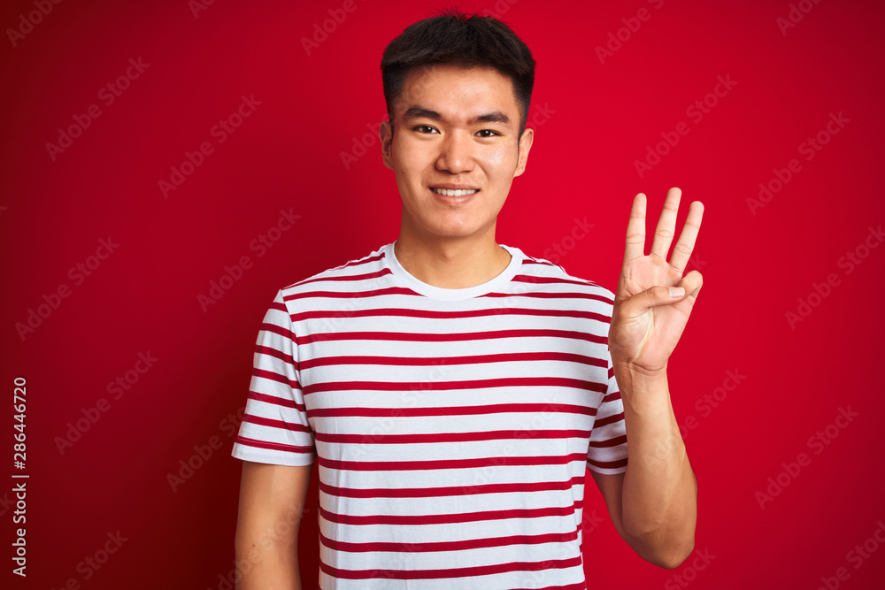Young asian chinese man wearing striped t-shirt standing over isolated red background showing and pointing up with fingers number three while smiling confident and happy. Young asian chinese man wearing striped t-shirt standing over isolated red background showing and pointing up with fingers number three while smiling confident and happy.