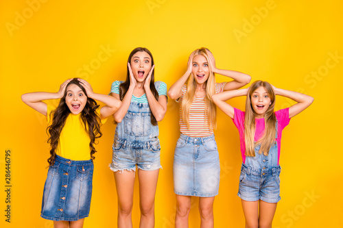 Photo of four cheerful with amazed facial expression open mouth shouting screaming ladies wearing denim overalls colorful t-shirts isolated bright background