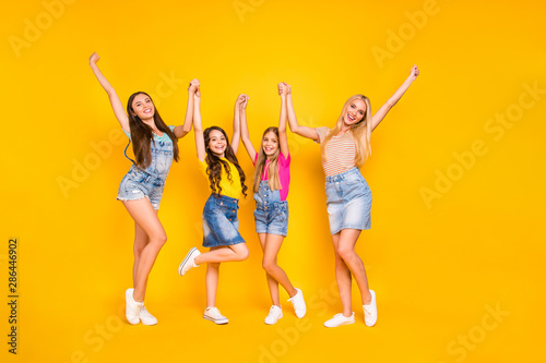 Full length body size photo of cheerful team of four members having great weekend and holidays wearing denim skirts outfit raising fists up isolated vibrant background