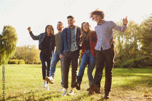 Young people laugh while standing in a park in spring.