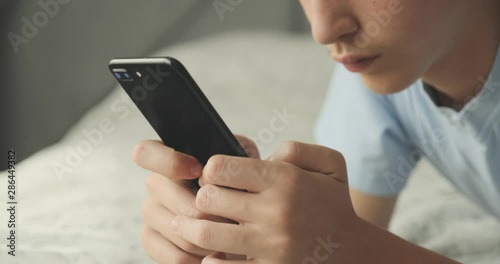 Teenager typing text message by smart phone, at home. Handsome boy spending time in a social network using mobile phone lying on sofa. Caucasian teenage guy talking on cell phone. Lifestyle concept.