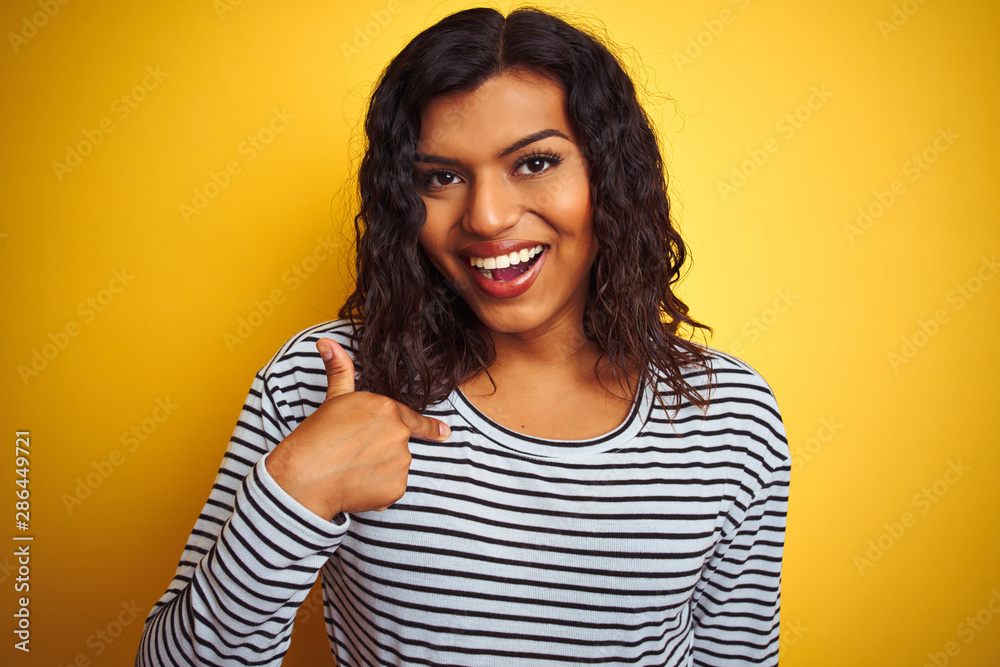 Transsexual transgender woman wearing striped t-shirt over isolated yellow background with surprise face pointing finger to himself Transsexual transgender woman wearing striped t-shirt over isolated yellow background with surprise face pointing finger to himself