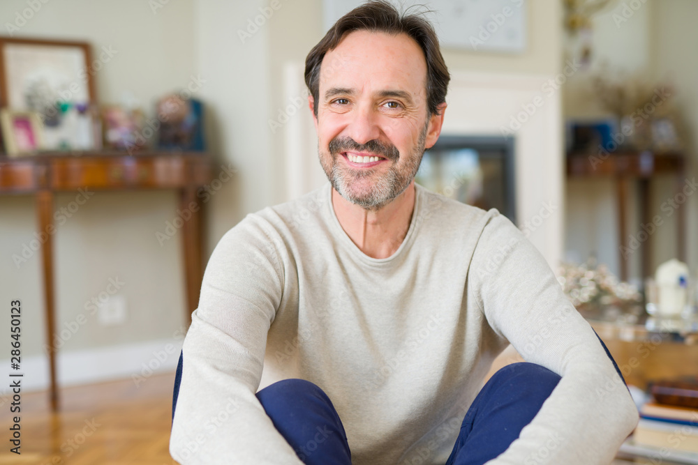 Handsome middle age man sitting on the floor smiling at the camera at home Handsome middle age man sitting on the floor smiling at the camera at home