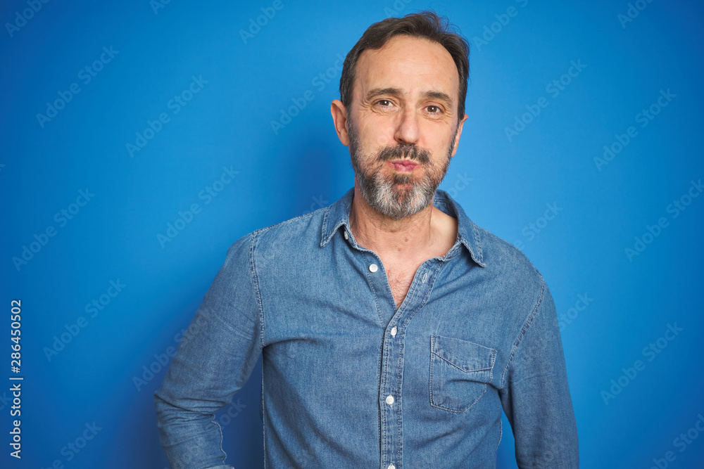 Obraz premium Handsome middle age senior man with grey hair over isolated blue background puffing cheeks with funny face. Mouth inflated with air, crazy expression.