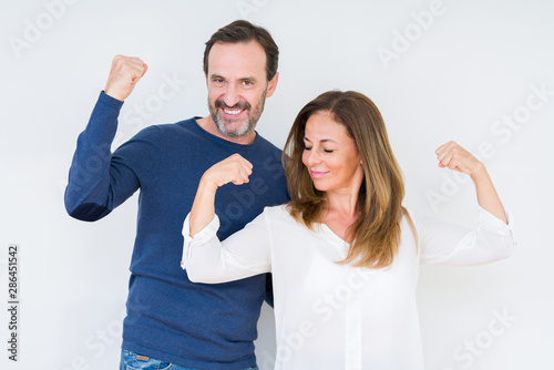Beautiful middle age couple in love over isolated background showing arms muscles smiling proud. Fitness concept.