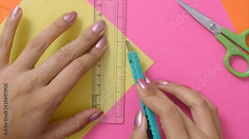 Overhead shot of a girl cutting a yellow chart paper with a cutter.  photo