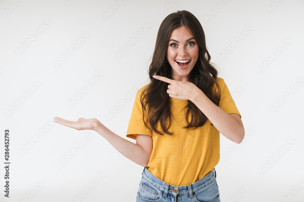 Image of amazed brunette woman wearing casual clothes smiling and pointing fingers at copyspace on her palm