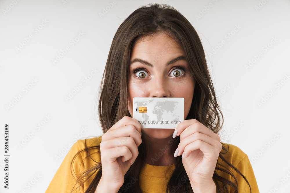 Image of surprised brunette woman wearing casual clothes holding credit card at her mouth Image of surprised brunette woman wearing casual clothes holding credit card at her mouth