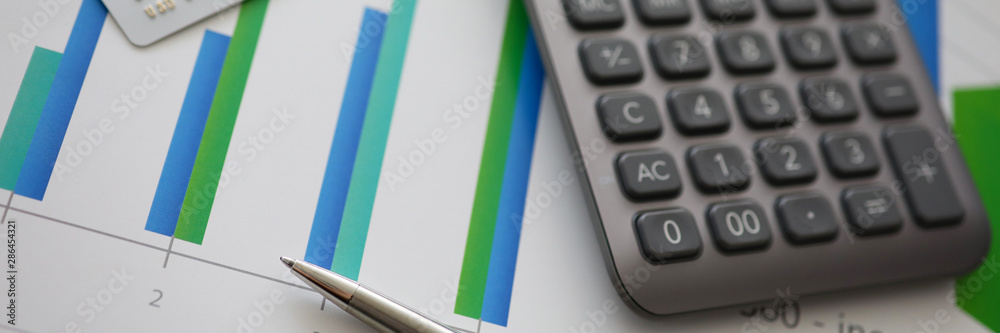 Silver pen gray calculator and credit plastic card lie on table aganist business chart background. Silver pen gray calculator and credit plastic card lie on table aganist business chart background.