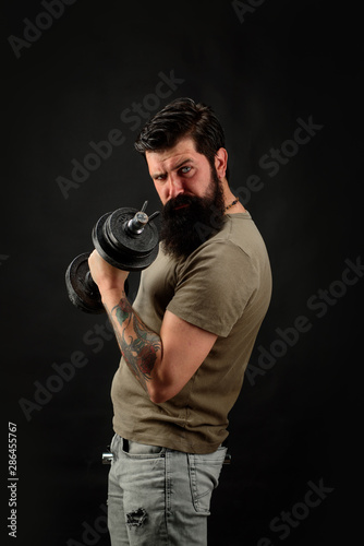 Athletic young male fitness model holds dumbbell. Fit young man in sportswear holds dumbbell during workout in gym. Healthy sports lifestyle, fitness concept. Handsome man lifting dumbbell at gym.