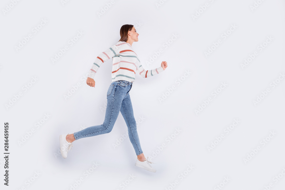 Full size profile side photo of pretty person running with beaming smile wearing striped sweater denim jeans isolated over white background