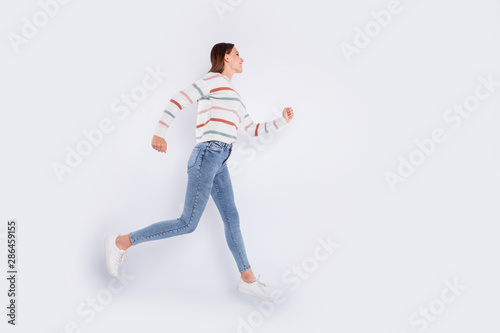 Full size profile side photo of pretty person running with beaming smile wearing striped sweater denim jeans isolated over white background