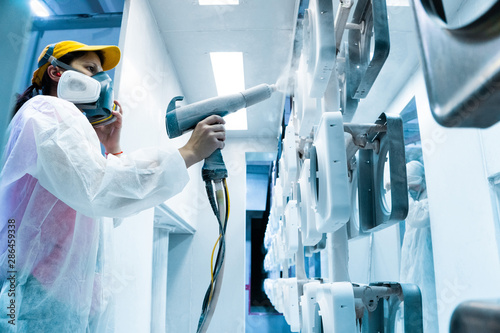 Powder coating of metal parts. A woman in a protective suit sprays white powder paint from a gun on metal products photo