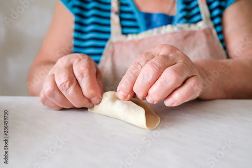 Old woman sculpts pasta. Grandma makes manti. Recipe for meat and dough.