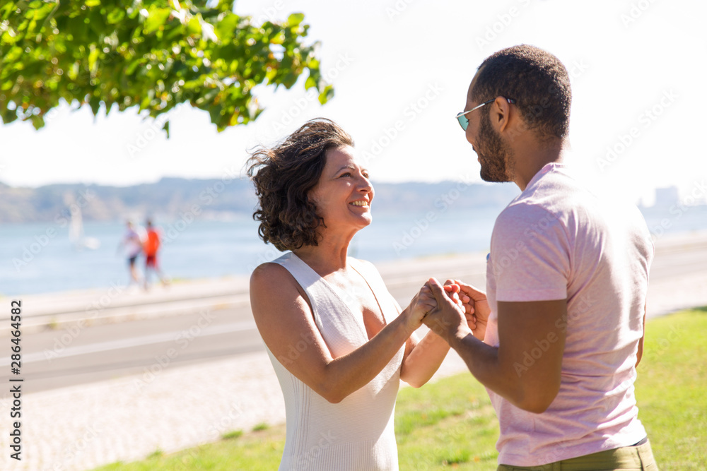 Cheerful couple meeting on promenade. Happy excited man and woman standing outdoors against each other, holding hands and smiling. Dating concept Cheerful couple meeting on promenade. Happy excited man and woman standing outdoors against each other, holding hands and smiling. Dating concept