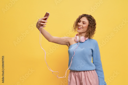 Glamour girl with headphones doing selfie, using phone.