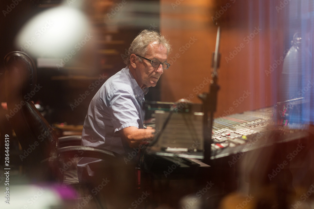 Male middle aged recording engineer in a recording studio sitting at a multi channel console Male middle aged recording engineer in a recording studio sitting at a multi channel console