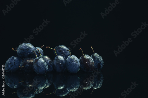 Beautiful fresh blue pulms on a black glass table and dark background. photo